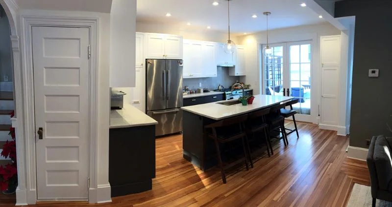 Complete kitchen cabinet installation with gray lower cabinets and white upper cabinets with minimalist Zephyr range hood.  Heartpine wood floor, premium baseboard and casings for trim.  Center island features low-profile countertop supports.